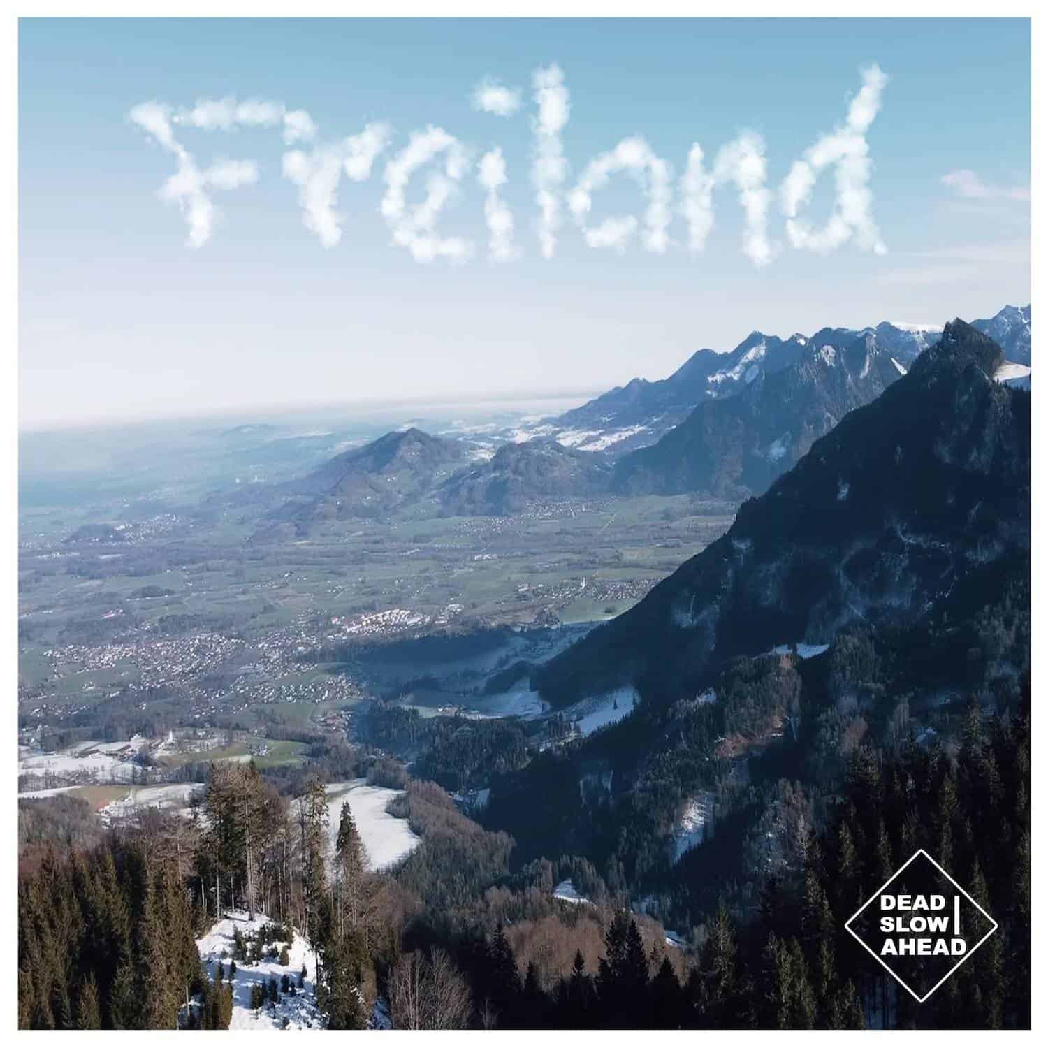 Blick auf Berge und Tal mit "Travel" Wolkenformation am Himmel, Musiklabel-Logo im unteren rechten B.